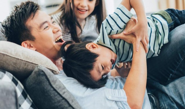 father plays on a couch with his young children
